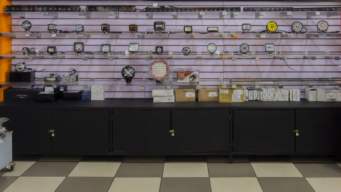 Display wall in the Repuestos Alto store with LED light bars and work lights on slatted panels above black cabinets.